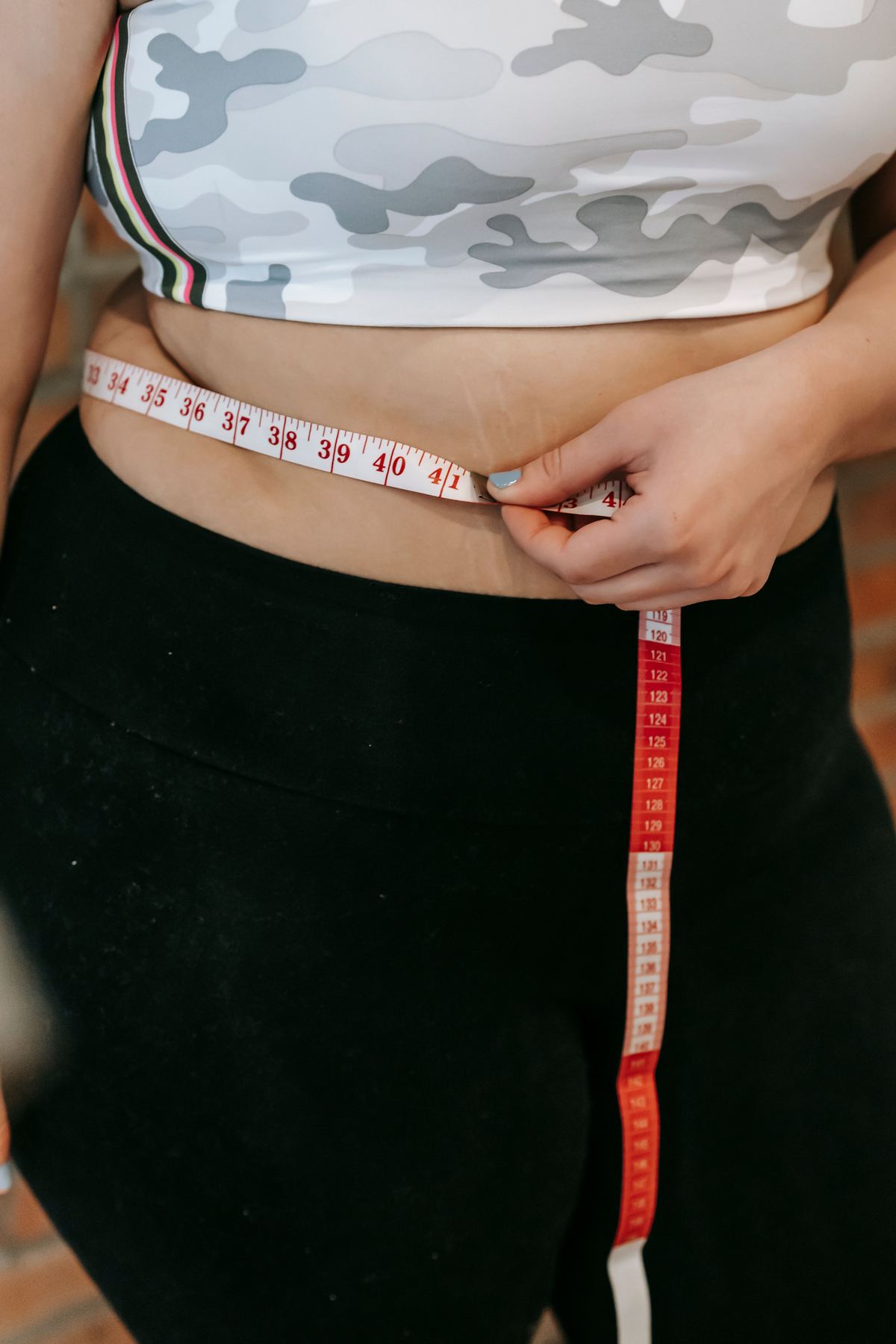 Person measuring their waist with a tape measure, tracking their progress